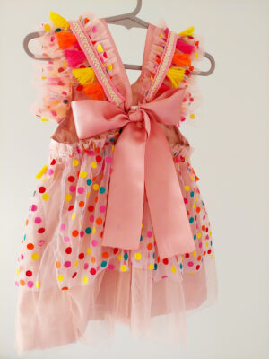 back view of a bright colour confetti spotted children's birthday party dress. This dress is handmade in New Zealand. A large pink bow ties the back of the dress.