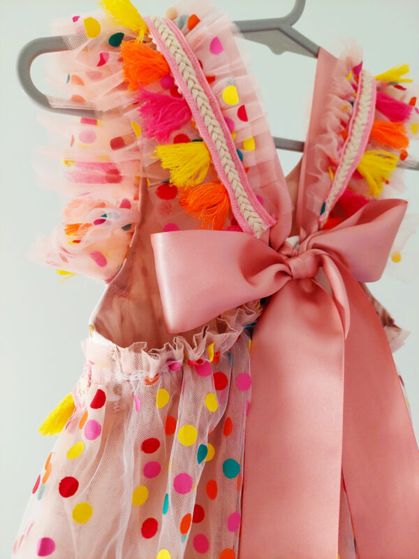 close up, back view of a bright colour confetti spotted children's birthday party dress. This dress is handmade in New Zealand. A large pink bow ties the back of the dress.