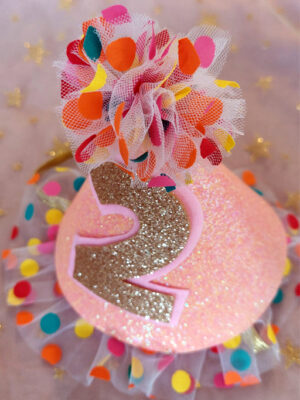 Top down view of a sparkling pink 'confetti' birthday party hat, with custom golden glitter number 2 displayed on the front.