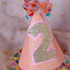 Sparkling pink 'confetti' birthday party hat, with custom golden glitter number 2 displayed on the front.