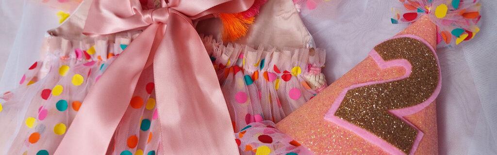 Pink and multicolour confetti spotted children's birthday party dress with a matching handmade sparkling fabric party hat. The hat displays the number 2 in golden glitter.