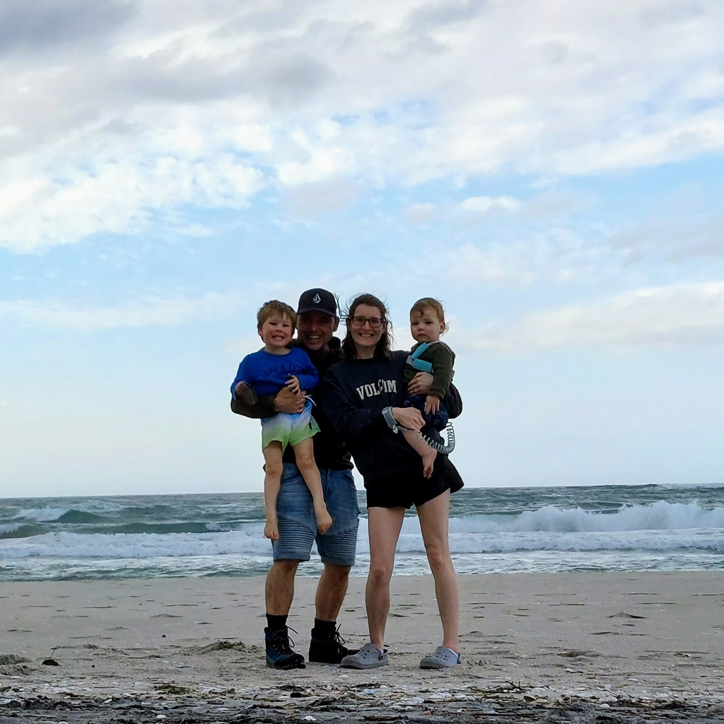 Owner of Mane and Tusk with her husband and two children smiling on the beach.