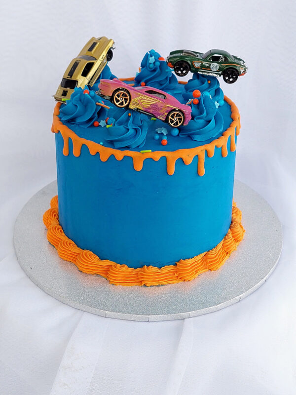 Racing car birthday cake with blue frosting, orange drip, and toy cars