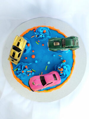 Racing car birthday cake with blue frosting, orange drip, and toy cars
